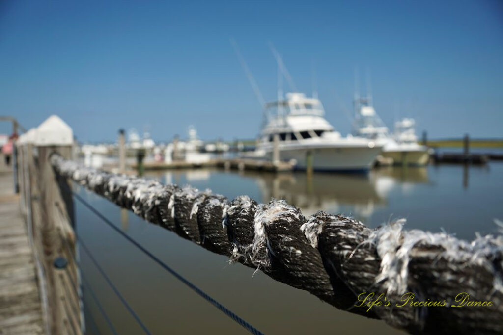 Close up of a frayed rope barrier along a pier. Fishing boats reflecting on the water in the background.