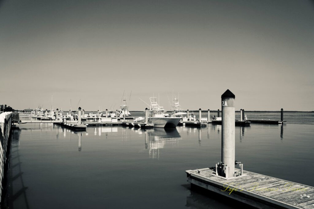 Black and white of fishing boats along docks, reflecting on the water, at The Marina at Edisto Island.