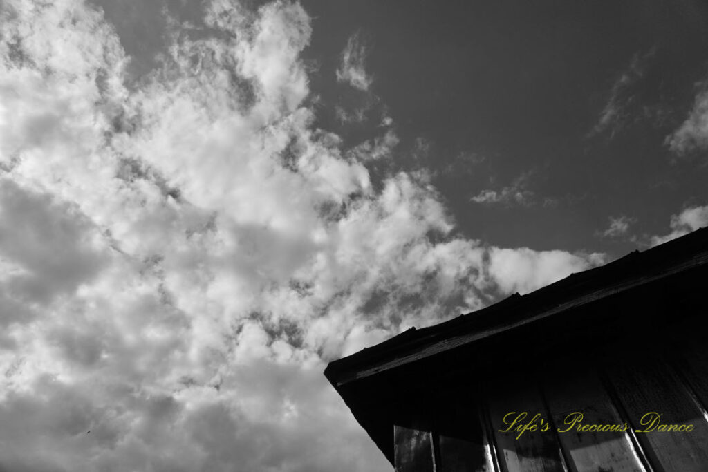 Black and white looking upward at the top corner of a barn, Passing clouds overhead.