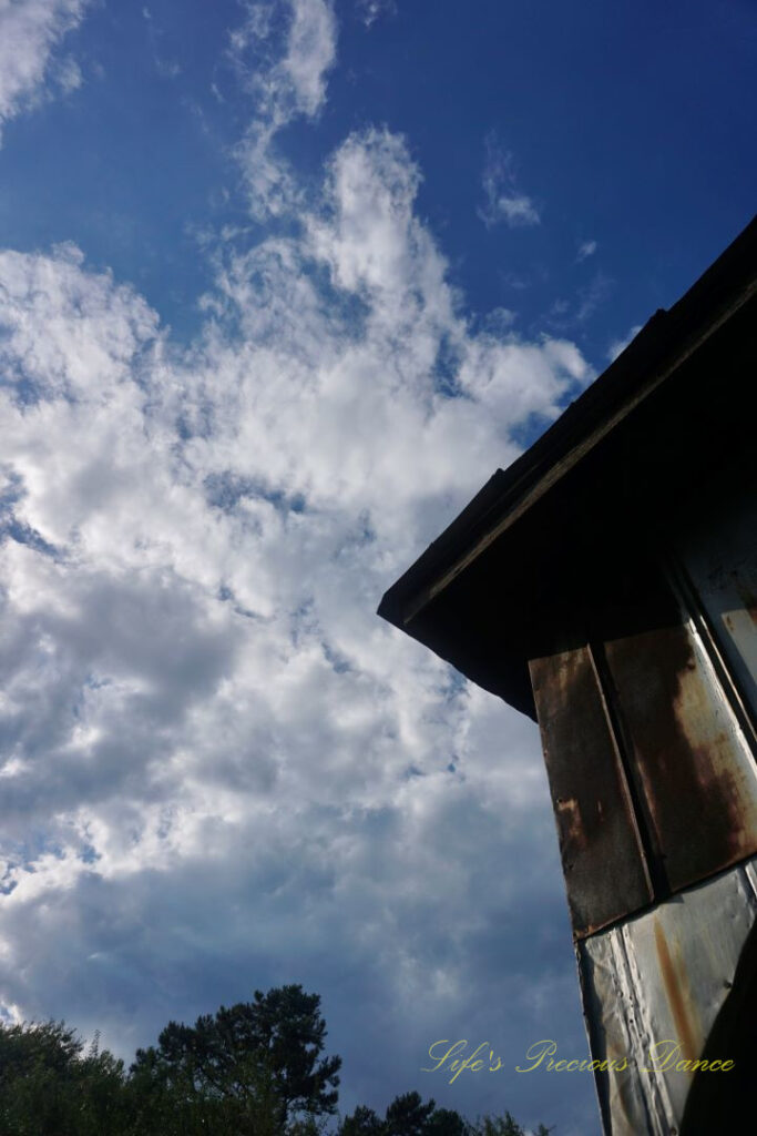 Looking upward at the top corner of a barn, Passing clouds overhead.