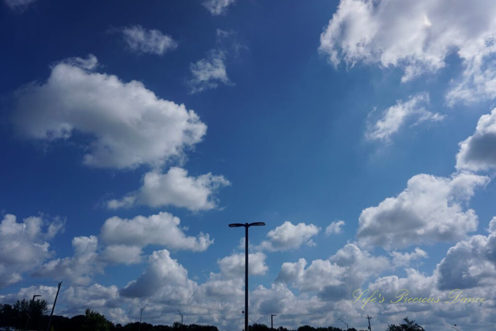 Fluffy passing clouds against a deep blue sky, A lone light pole in the center.