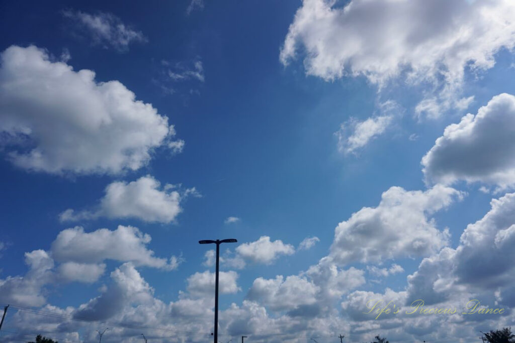 Fluffy passing clouds against a deep blue sky, A lone light pole in the center.