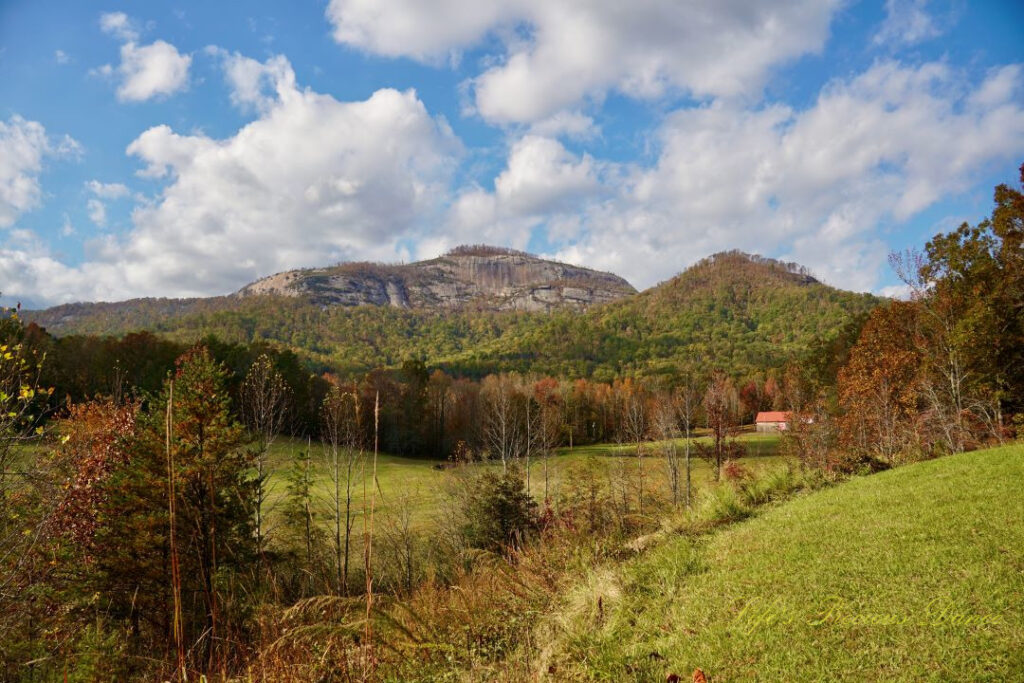 Landscape view of Table Rock and the surrounding mountain range from Grant Meadow Overlook. Passing fluffy clouds overhead. A small ranch house can be seen to the right.