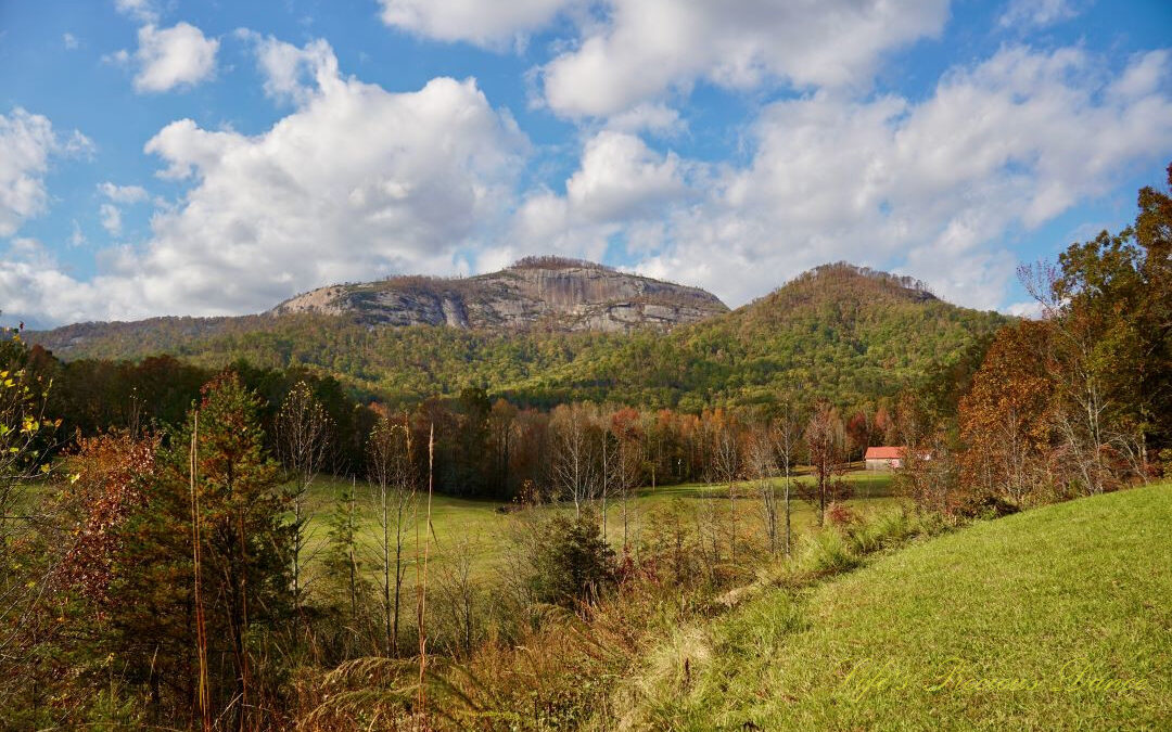 Landscape view of Table Rock and the surrounding mountain range from Grant Meadow Overlook. Passing fluffy clouds overhead. A small ranch house can be seen to the right.