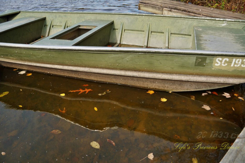 Rowboat tied to a dock, reflecting on the water&#039;s surface amongst floating leaves.