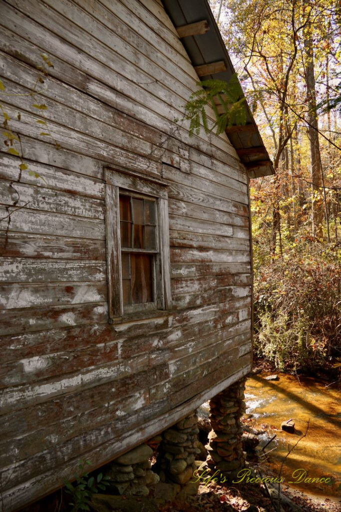 Side of GIlreath&#039;s MIll. featuring a window with missing glass. Colorful trees in the background