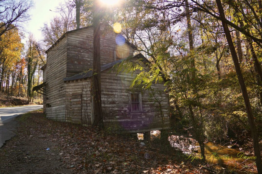 Front and side view of historic Gilreath&#039;s Mill. The creek in the background, trees and road to the left and the sun&#039;s colorful photons shing down across the center.