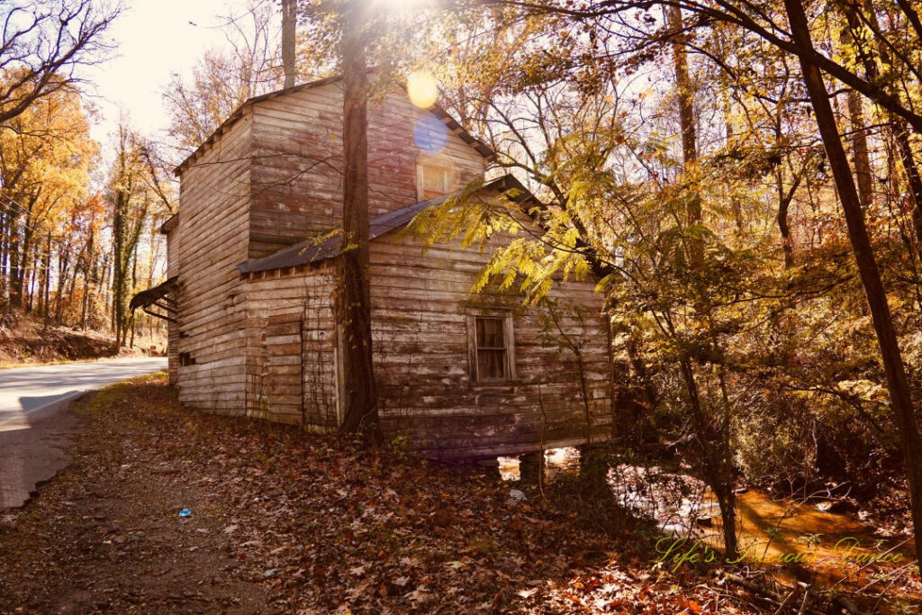 Front and side view of historic Gilreath&#039;s Mill. The creek in the background, trees and road to the left and the sun&#039;s colorful photons shing down across the center.