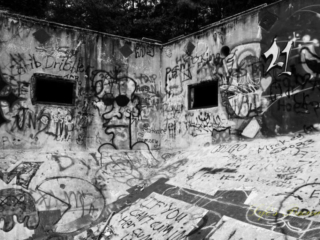 Black and white view from the deep end, looking upward at the graffiti covered corner of Springs Recreation Pool. Two windows in the walls.
