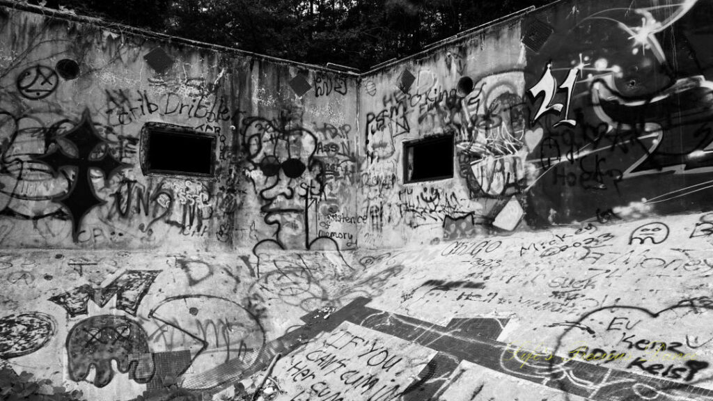 Black and white view from the deep end, looking upward at the graffiti covered corner of Springs Recreation Pool. Two windows in the walls.