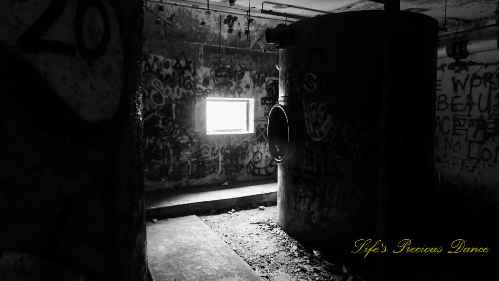 Black and white of the graffiti covered pump room, located below the water level at abandoned Springs pool. A viewing window can be seen on a backwall.