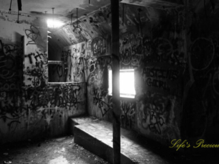 Black and white of the graffiti covered pump room, located below the water level at abandoned Springs pool. A viewing window on a back wall.