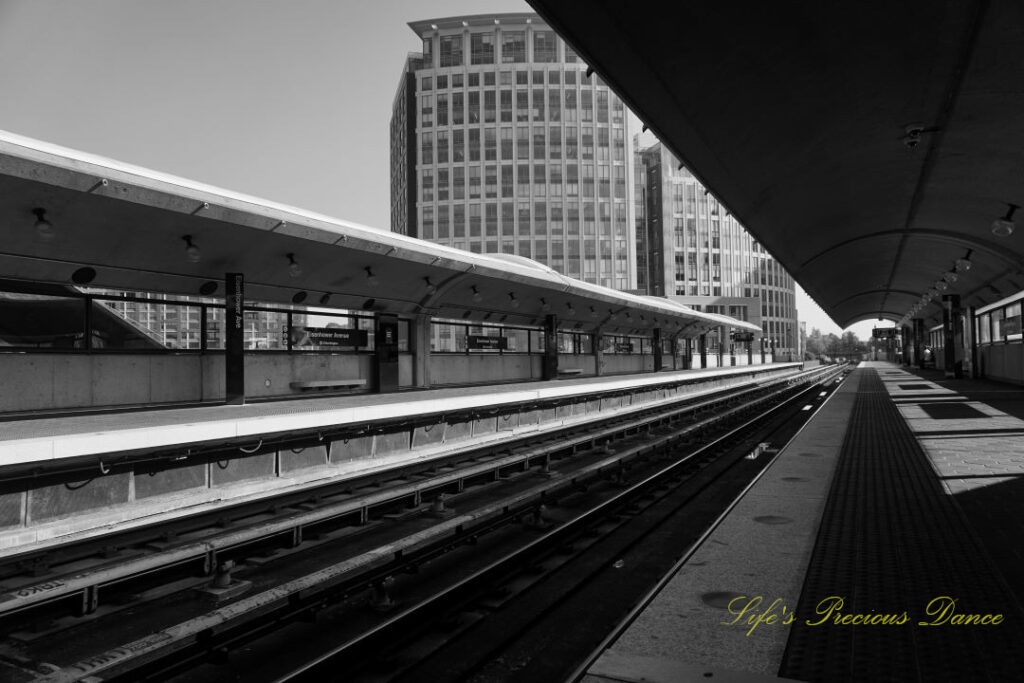 Black and white street level view of the train tracks at the DC Metro station. A tall building in the background.