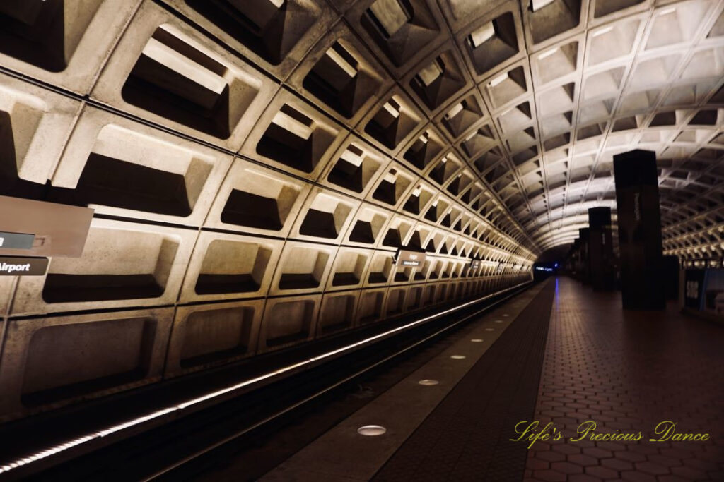 Looking down the track of the tunnel at DC Metro station. The lights of an approaching train can be seen in the distance.