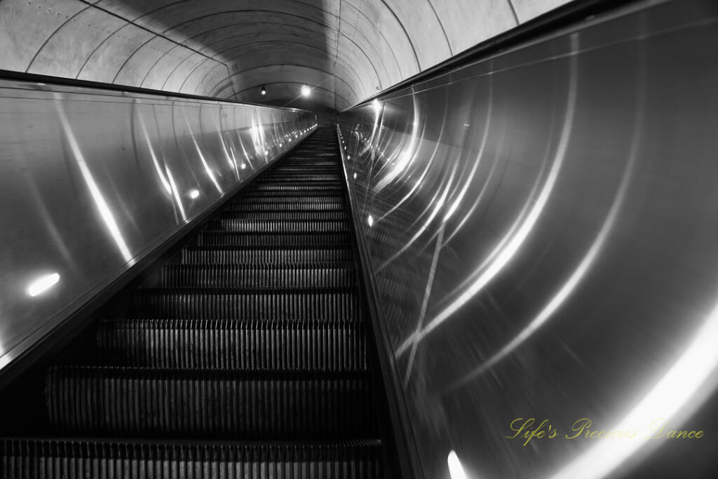 Black and white ground level view, looking upward at a extremely long escalator rising