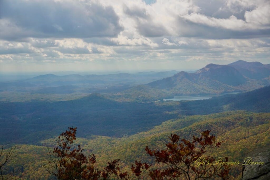 Landscape view from Caesars Head overlook. The suns rays cascade through overhead passing clouds and a lake can be seen in between the mountain ranges.