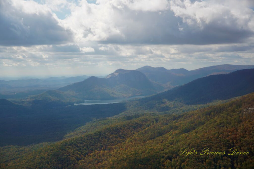 Landscape view from Caesars Head overlook. The suns rays cascade through overhead passing clouds and a lake can be seen in between the mountain ranges.