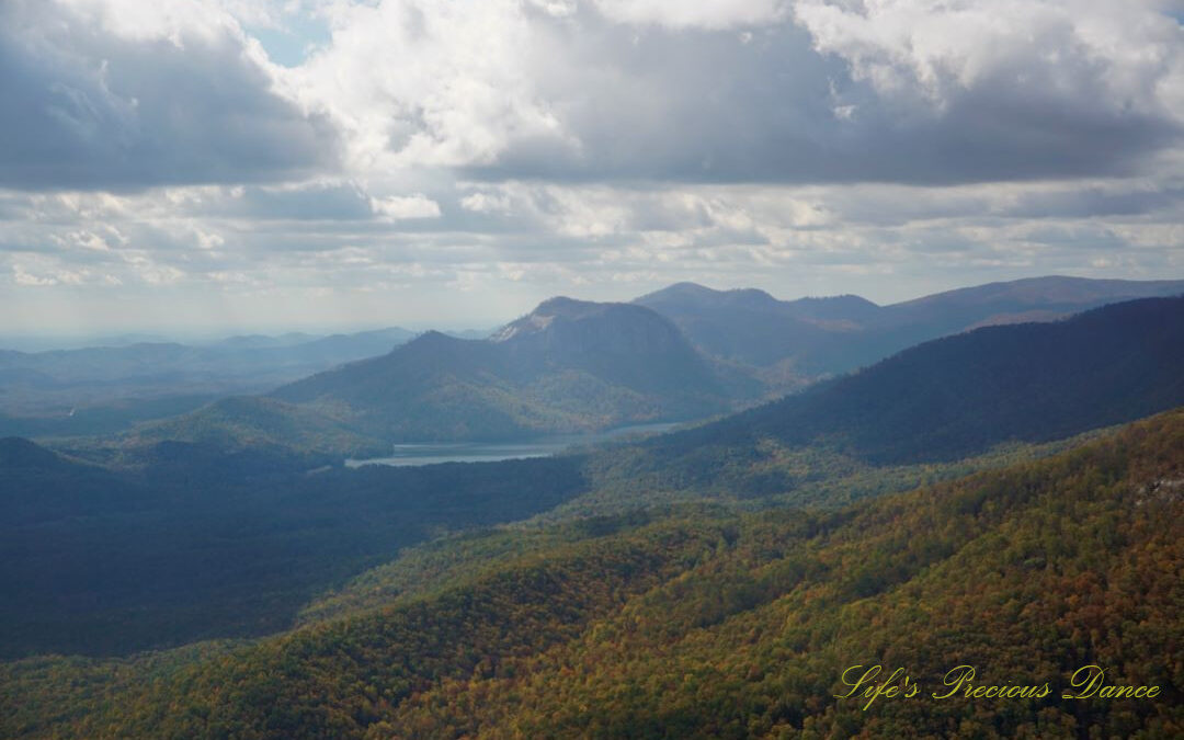 Landscape view from Caesars Head overlook. The suns rays cascade through overhead passing clouds and a lake can be seen in between the mountain ranges.