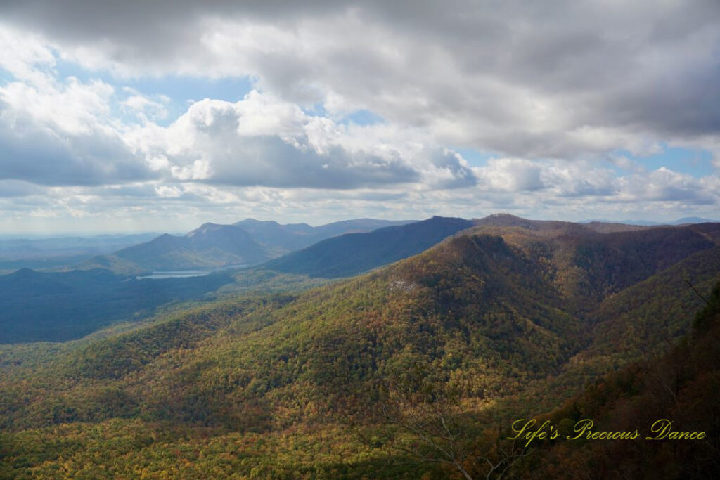 Landscape view from Caesars Head overlook. The suns rays cascade through overhead passing clouds and a lake can be seen in between the mountain ranges.