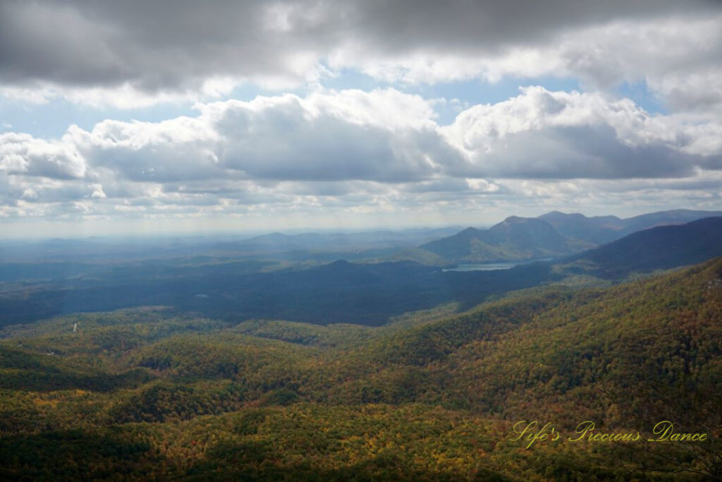 Landscape view from Caesars Head overlook. The suns rays cascade through overhead passing clouds and a lake can be seen in between the mountain ranges.