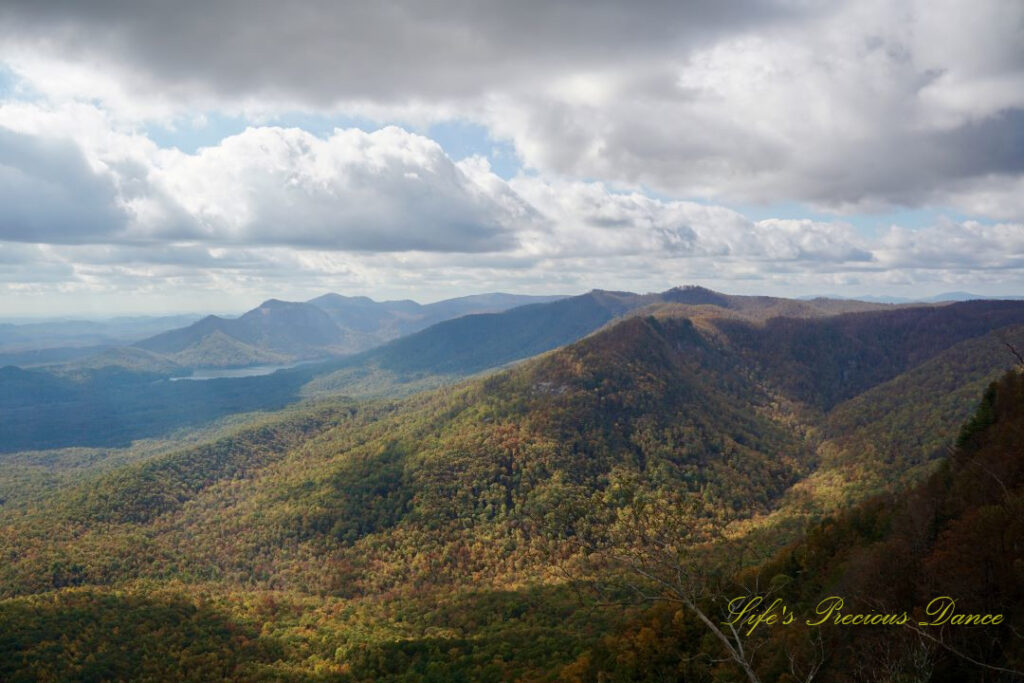 Landscape view from Caesars Head overlook. The suns rays cascade through overhead passing clouds and a lake can be seen in between the mountain ranges.