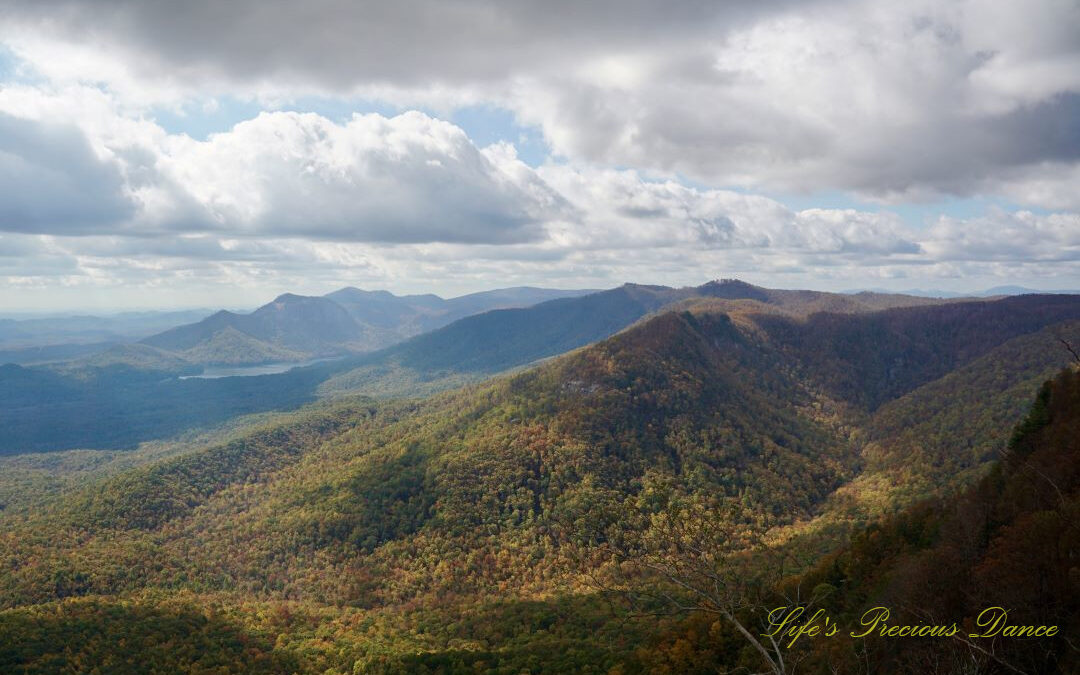 Landscape view from Caesars Head overlook. The suns rays cascade through overhead passing clouds and a lake can be seen in between the mountain ranges.