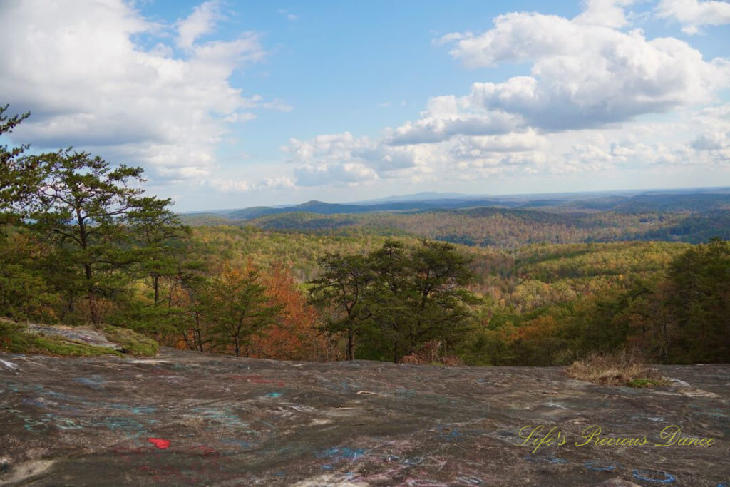 Landscape view from Bald Rock looking outward at mountain ranges and valleys. Passing clouds overhead. Graffiti can be seen on the rockface.