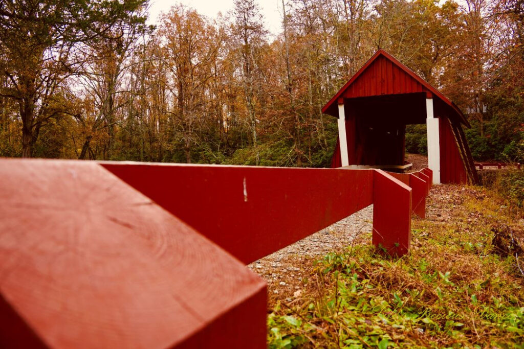 Ground level view of the frontside of Campbell&#039;s Covered Bridge and the wooden guard rail leading to it.