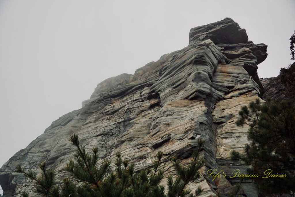 Looking upward at the jagged face of Pilot Mountain. Cloudy, foggy sky above.