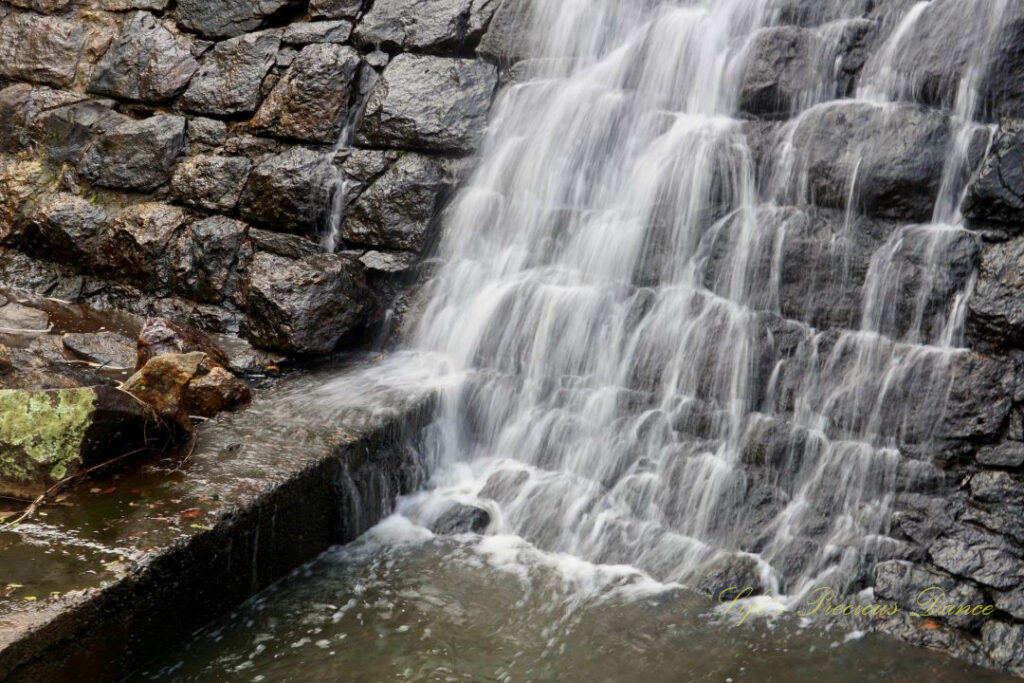 Close up of the base of a waterfall, flowing down a rockwall into an awaiting creek.