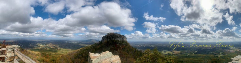 Panoramic view of Pilot Mountain. Fluffy clouds overhead and surrounded by distant mountain peaks and valleys